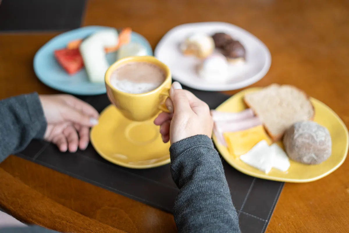 Café da manhã servido à mesa, com cappuccino, pães, frios e frutas